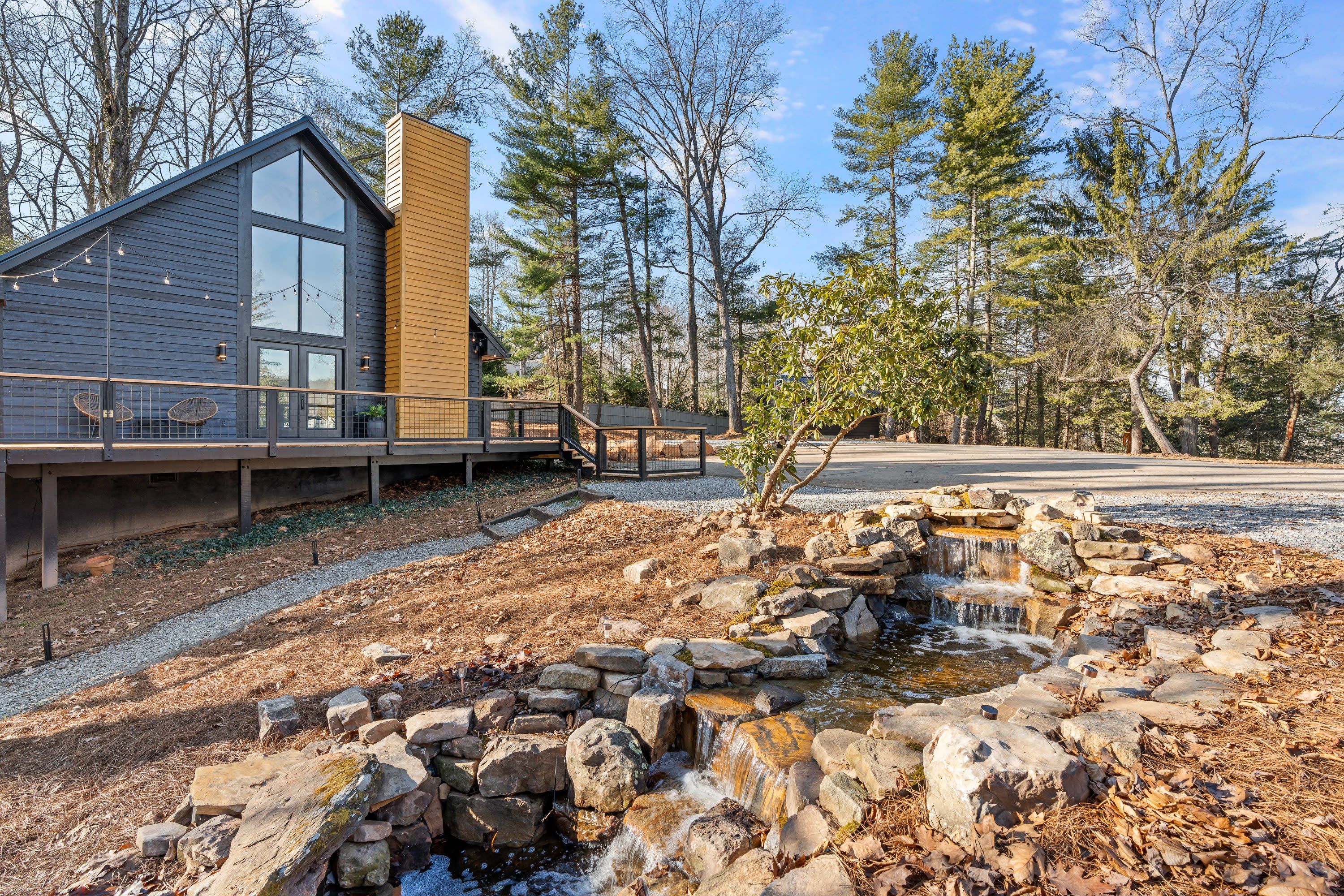 A modern house with a wooden deck and a stone waterfall feature.