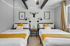 Ein Zimmer mit zwei Betten, einer Holzbalkendecke, einem aufgehängten Hirschgeweih, gerahmten Kunstwerken und einem Nachttisch mit Lampe.