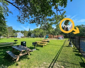 Ein Park mit Picknicktischen, einem Spielplatz und einem Schwimmbadbereich.