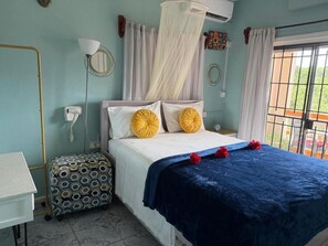 A bedroom with a bed, a bedside table, a small stool, a window with curtains, and a mosquito net. - Cozy 1-bedroom apartment in fantastic Castries with AC (Monchy)