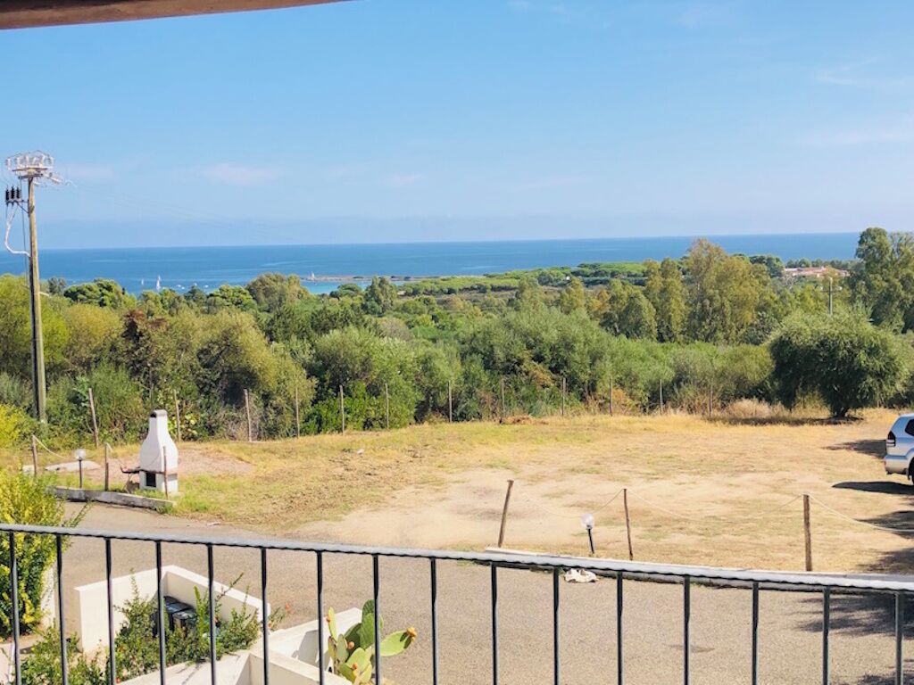 A view of a coastal landscape with a clear sky, a body of water in the distance, and a parking area with a fence in the foreground.