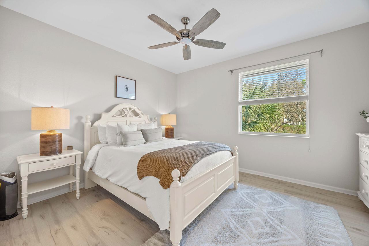 A bedroom with a bed, nightstands, a ceiling fan, a window with a view, and a white dresser.