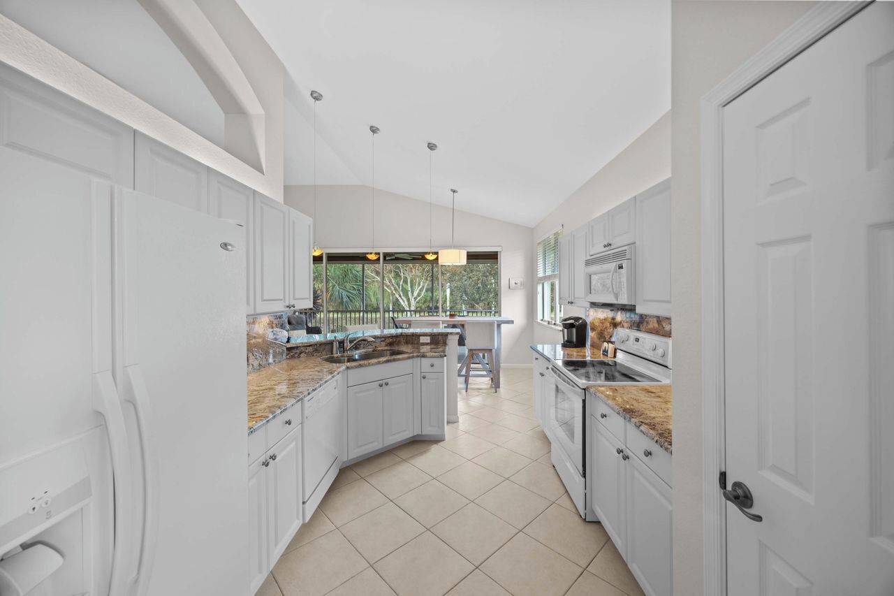 A modern kitchen with white cabinetry, granite countertops, and a large window providing a view of greenery.