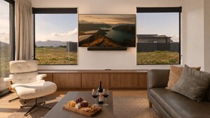 En moderne stue med et stort vindue, en hvid sofa, en lædersofa, et træbord med en ostebakke, vinglas og to landskabsmalerier.