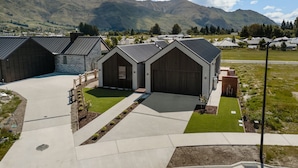 En moderne bygning med store garageporte, en velplejet græsplæne og et bjergrigt landskab i baggrunden.