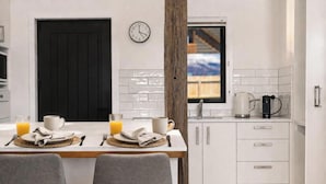 A modern kitchen with white cabinets, a black door, a clock, and a window with a view. - Central Wanaka Escape | Lake Views | Walk to Town | Deck & BBQ (Wānaka)