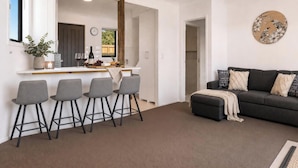 A modern living room with a dark grey sofa, a coffee table, and a bar area with stools. - Central Wanaka Escape | Lake Views | Walk to Town | Deck & BBQ (Wānaka)