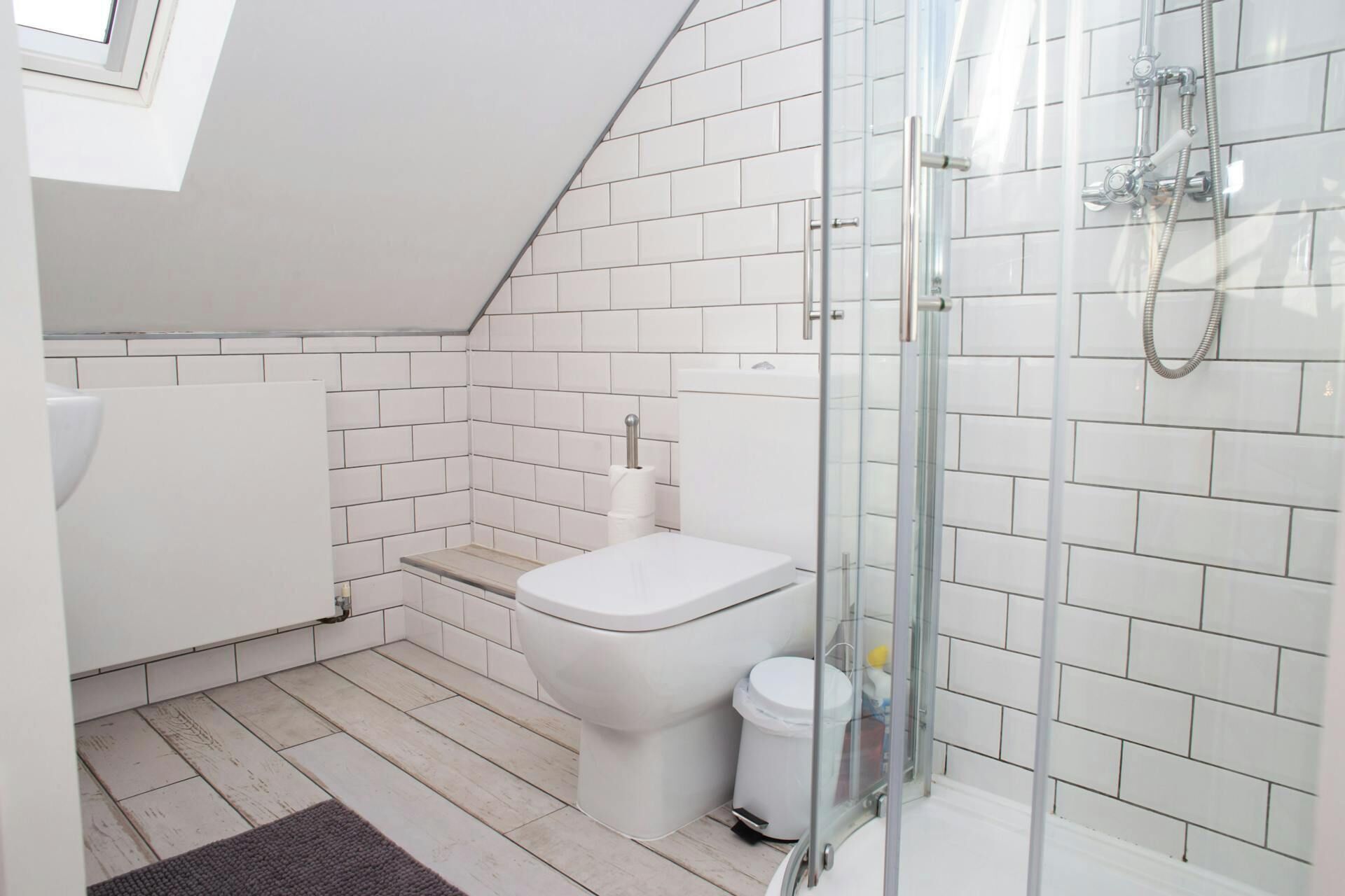 Un baño moderno con inodoro, ducha y paredes cubiertas de azulejos blancos.