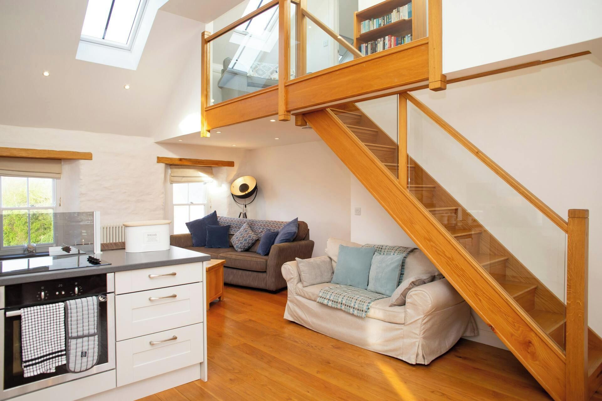 A spacious living area with a wooden staircase, a kitchen with a built-in oven, and a large window providing natural light.