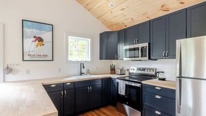Une cuisine moderne avec des meubles de couleur sombre, des appareils électroménagers en acier inoxydable et un plafond en bois.