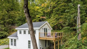 Une maison à deux étages avec un balcon, entourée d’arbres.