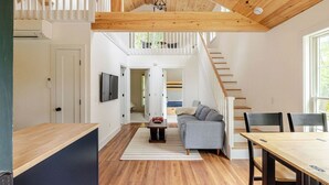 Un vaste espace de vie comprenant un escalier, un canapé, une table à manger et un téléviseur fixé au mur.