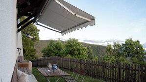 Un pati amb taula i cadires, una tanca de fusta i vistes a una zona boscosa.