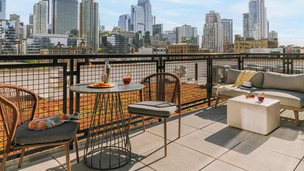 A rooftop terrace with a city skyline view, furnished with wicker chairs, a round table, and a sofa. - Luxury Penthouse Loft w/Terrace  507 | River North (Chicago)