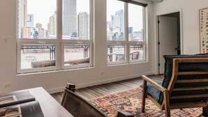 A spacious room with large windows offering a city view, a wooden chair, and a patterned rug. - Luxury Penthouse Loft w/Terrace  507 | River North (Chicago)