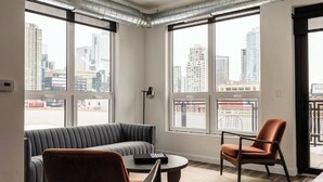 A modern living room with a sofa, a chair, and a coffee table. Large windows offer a view of the city skyline. - Luxury Penthouse Loft w/Terrace  504 | River North (Chicago)