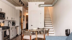 A compact kitchen with modern appliances, a dining area with a round table and chairs, and a staircase leading to another level. - Luxury Penthouse Loft w/Terrace  504 | River North (Chicago)