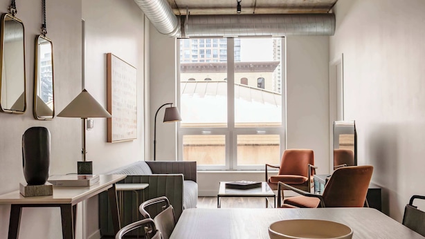 A modern living room with a dining table, chairs, a sofa, and a large window offering a view of buildings. - Luxury Designer Loft 302 | River North (Chicago)