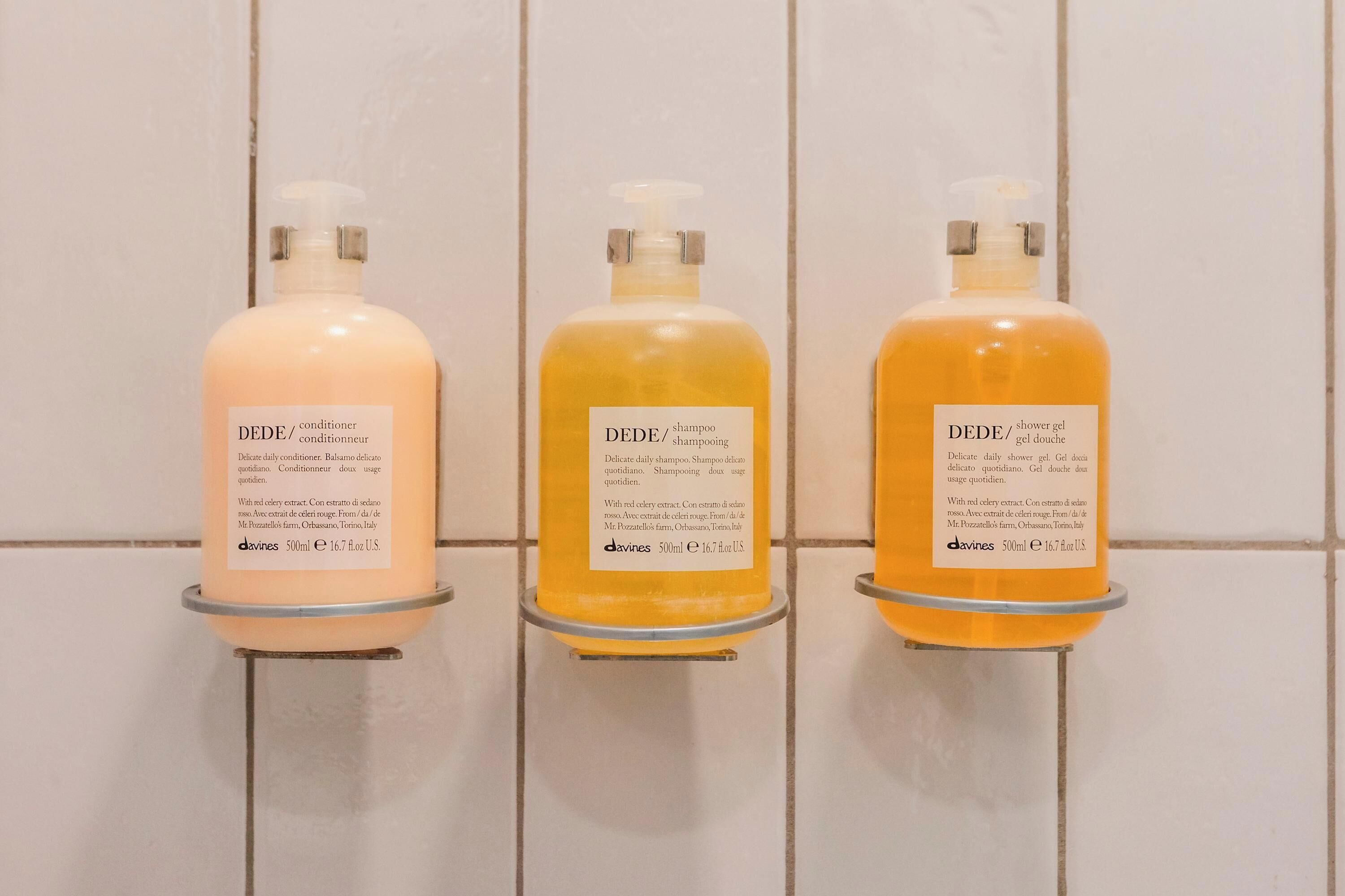 Three bottles of DEDE products on a tiled wall.