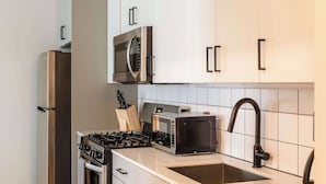 A modern kitchen with white cabinets, stainless steel appliances, a dishwasher, and a tiled backsplash. - Luxury Designer Loft 302 | River North (Chicago)