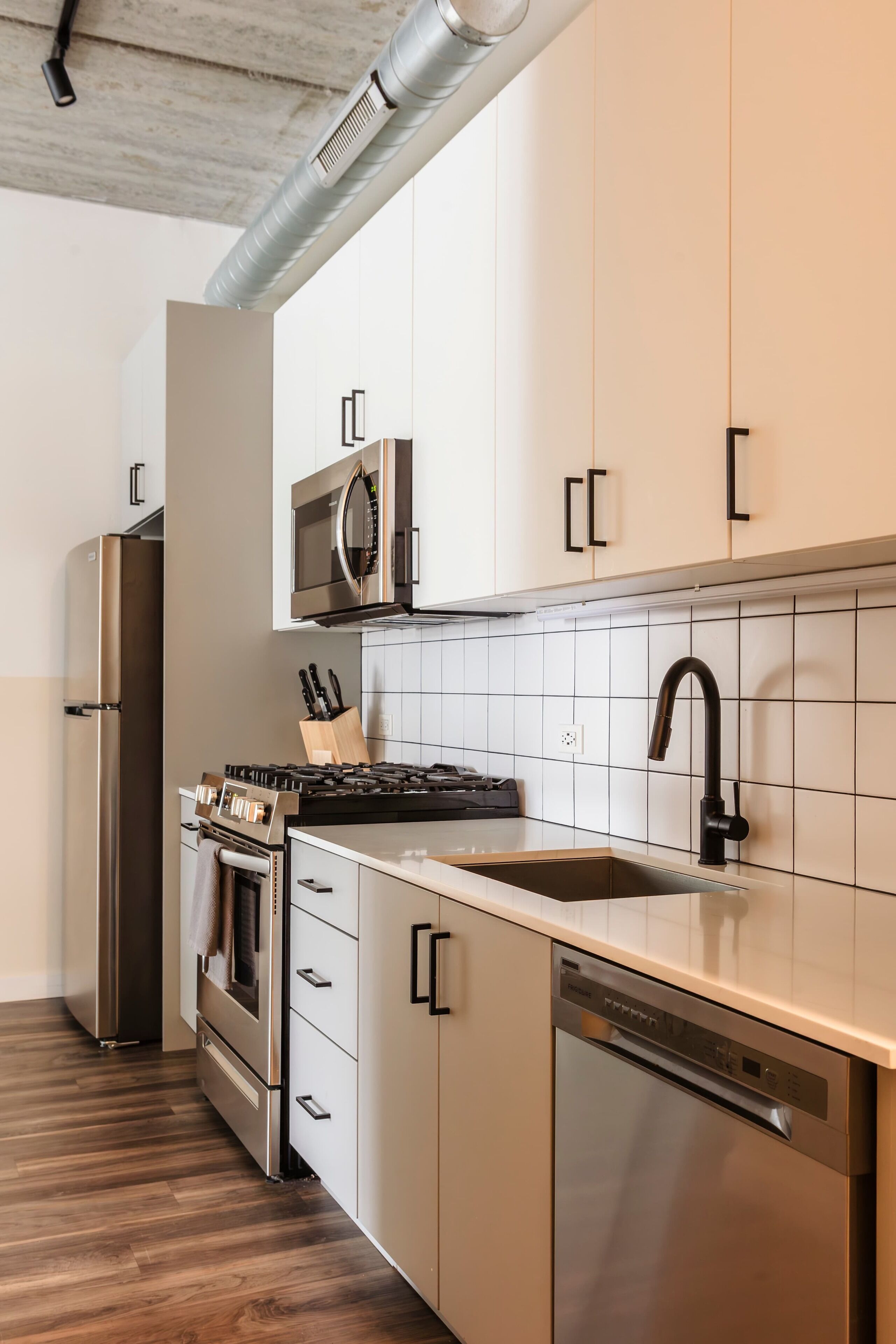 A modern kitchen with stainless steel appliances, white cabinetry, and a tiled backsplash.
