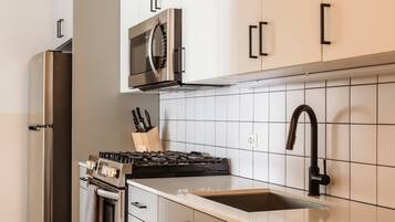 A modern kitchen with stainless steel appliances, white cabinetry, and a tiled backsplash.
