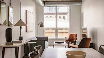 A modern living room with a dining table, chairs, a sofa, and a large window offering a view of buildings.