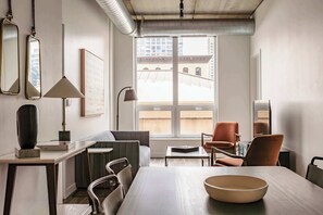 Ein modernes Wohnzimmer mit Esstisch, Stühlen, einer Couch und einem großen Fenster mit Blick auf Gebäude.