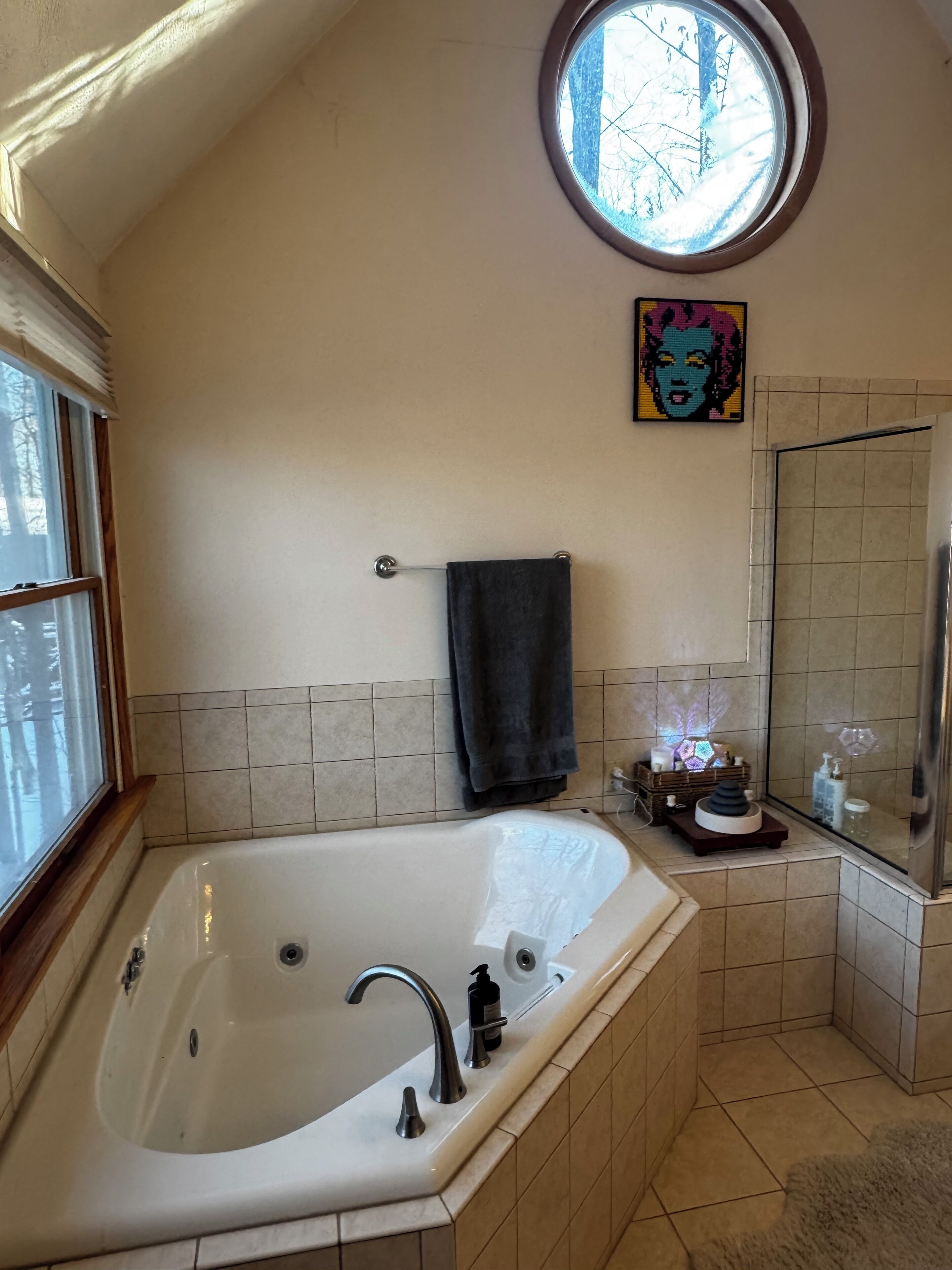 Une salle de bain avec une grande baignoire, une fenêtre, un porte-serviettes, un miroir et un objet décoratif accroché au mur.