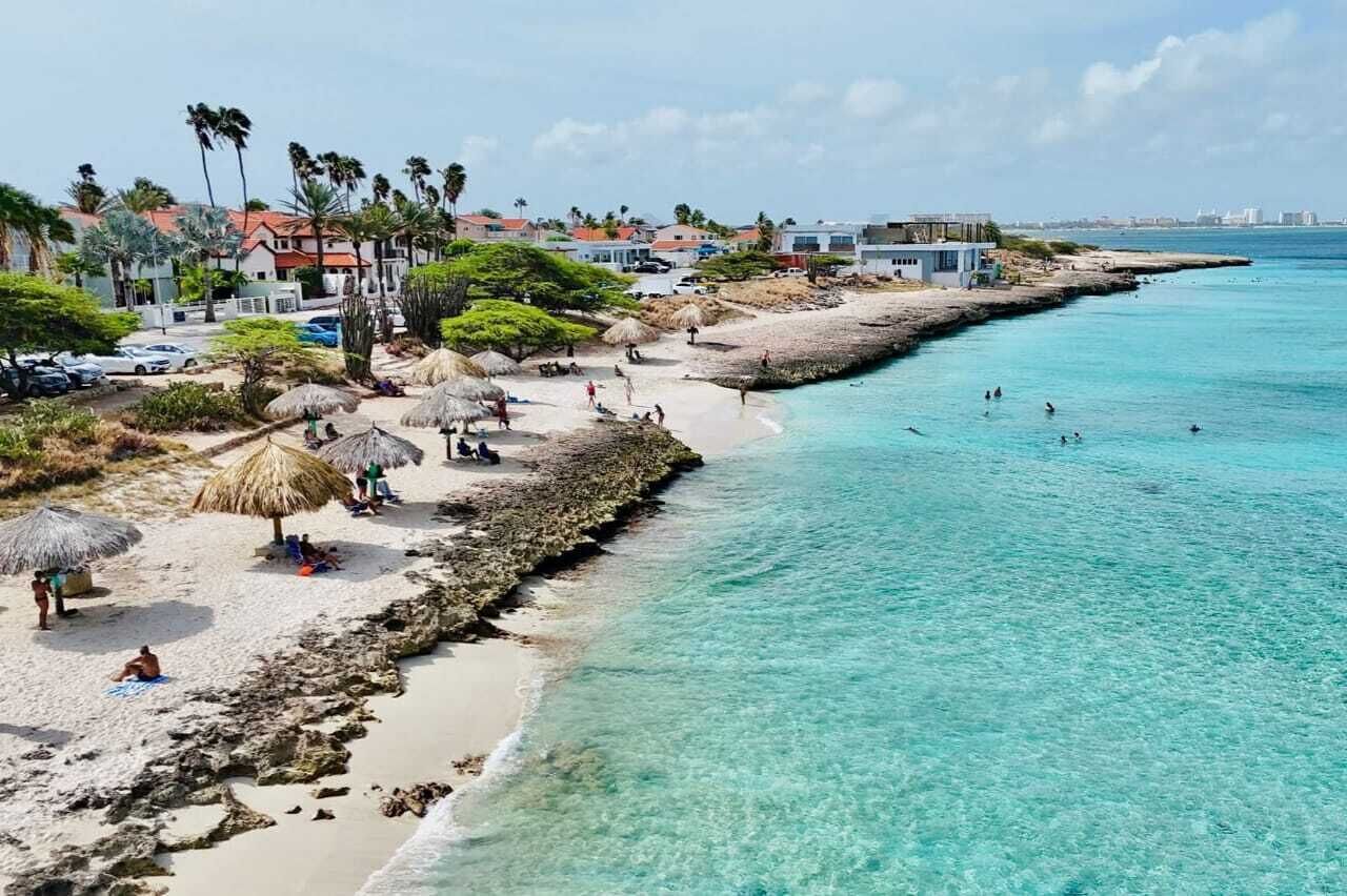 Una playa con agua turquesa cristalina, palmeras y sombrillas.