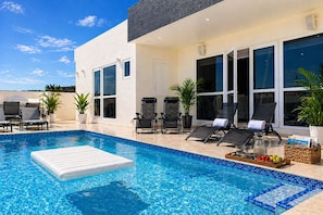 A modern pool area with a clear blue pool, lounge chairs, and potted plants.
