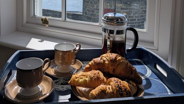 A tray with a coffee pot, a cup, and pastries by a window with a view of the sea.