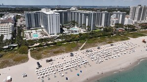 Een hoog hotel met meerdere verdiepingen, een strand met veel ligbedden en een zwembad.
