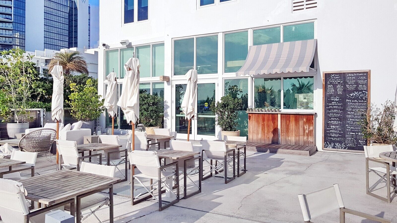 An outdoor seating area with tables and chairs, a wooden bar, and a chalkboard menu.