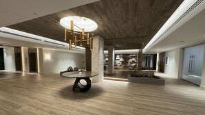 Een ruime lobby met een moderne kroonluchter, een ronde tafel en een stenen accentmuur.