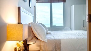 Een slaapkamer met een bed, nachtkastje, lamp, raam met jaloezieën en een kledingkast.