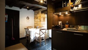 Un coin repas chaleureux avec un mur en pierre, des poutres en bois au plafond et une table blanche dressée pour deux personnes.