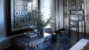 Une citation encadrée accrochée au mur, un vase rempli de fleurs, des livres et une vieille valise.