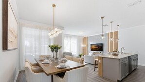 Eine moderne Küche mit einer zentralen Kochinsel, einem Essbereich mit Holztisch und -stühlen sowie einem Wohnbereich mit Sofa und Fernseher.