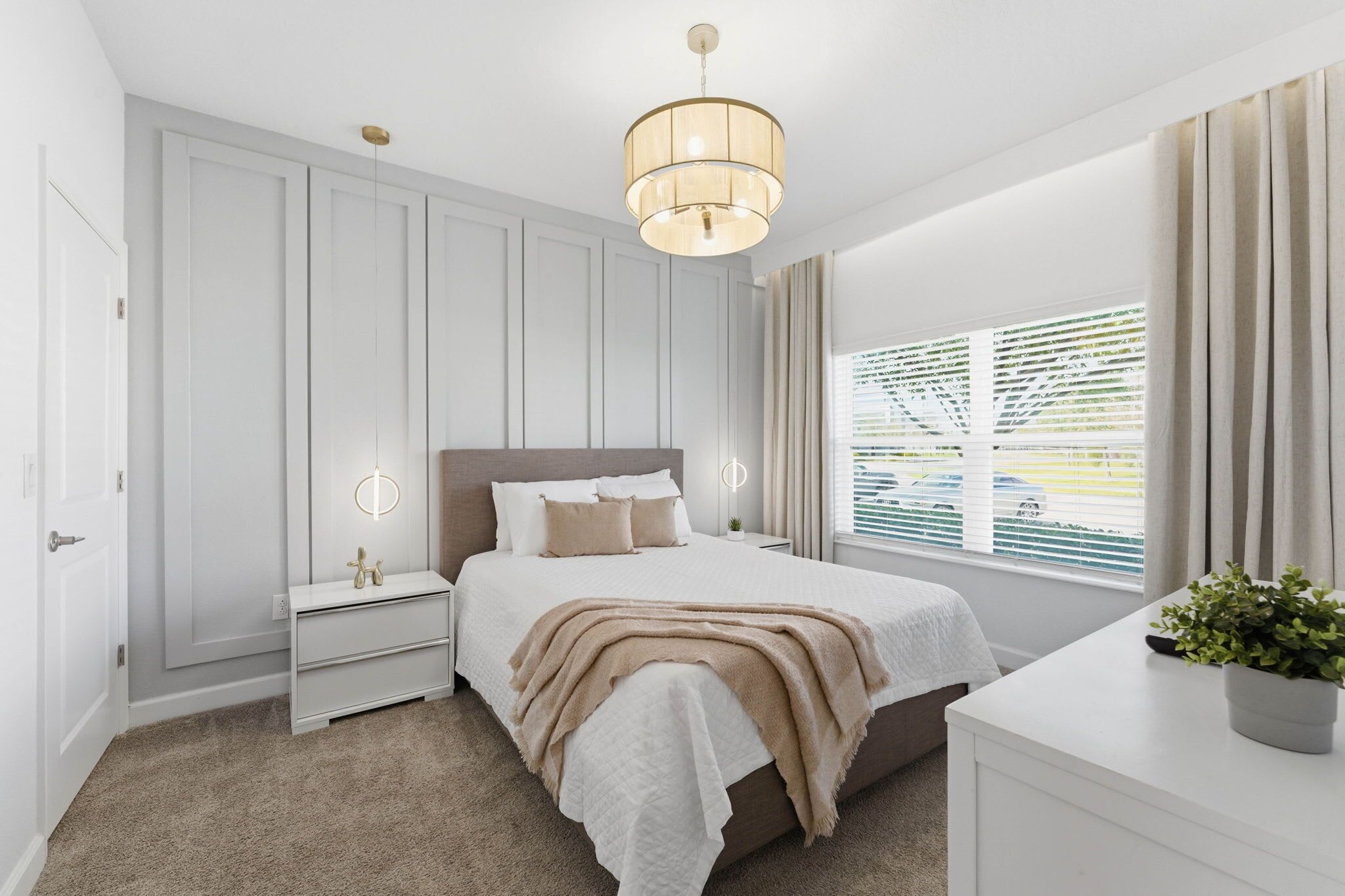 A bedroom with a bed, bedside tables, a nightstand, a window with blinds, and a ceiling light fixture.