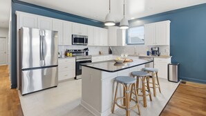 A modern kitchen with white cabinets, stainless steel appliances, a central island with stools, and pendant lighting. - Golf Sim, Theater, Games, Walk to Beach, Sleeps 28 (North Myrtle Beach)