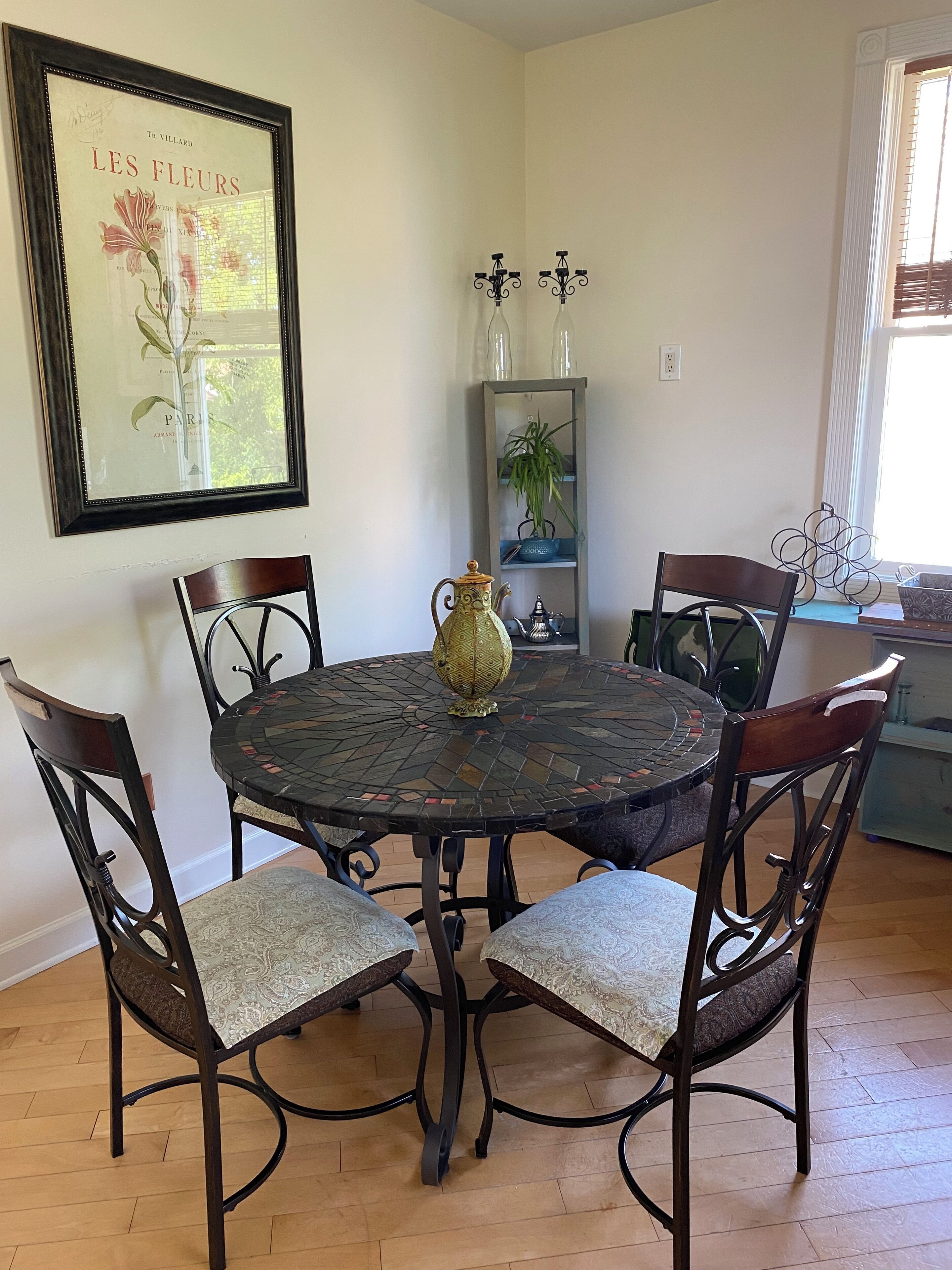 Un coin repas comprenant une table ronde, six chaises, un vase décoratif et un tableau encadré accroché au mur.