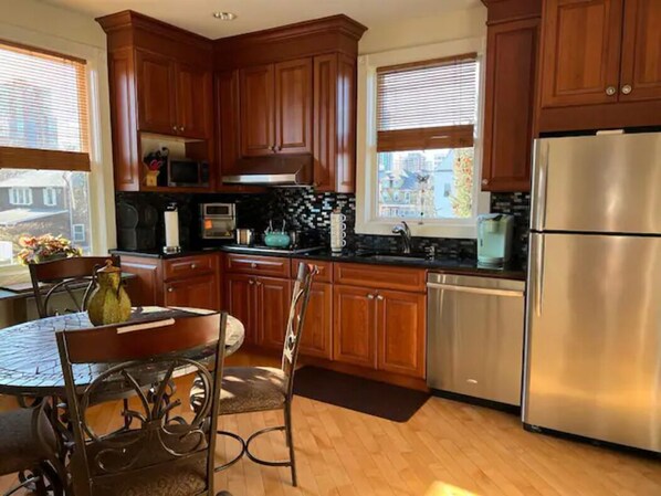 Una cocina con armarios de madera, electrodomésticos de acero inoxidable y un comedor con una silla y una mesa de metal.