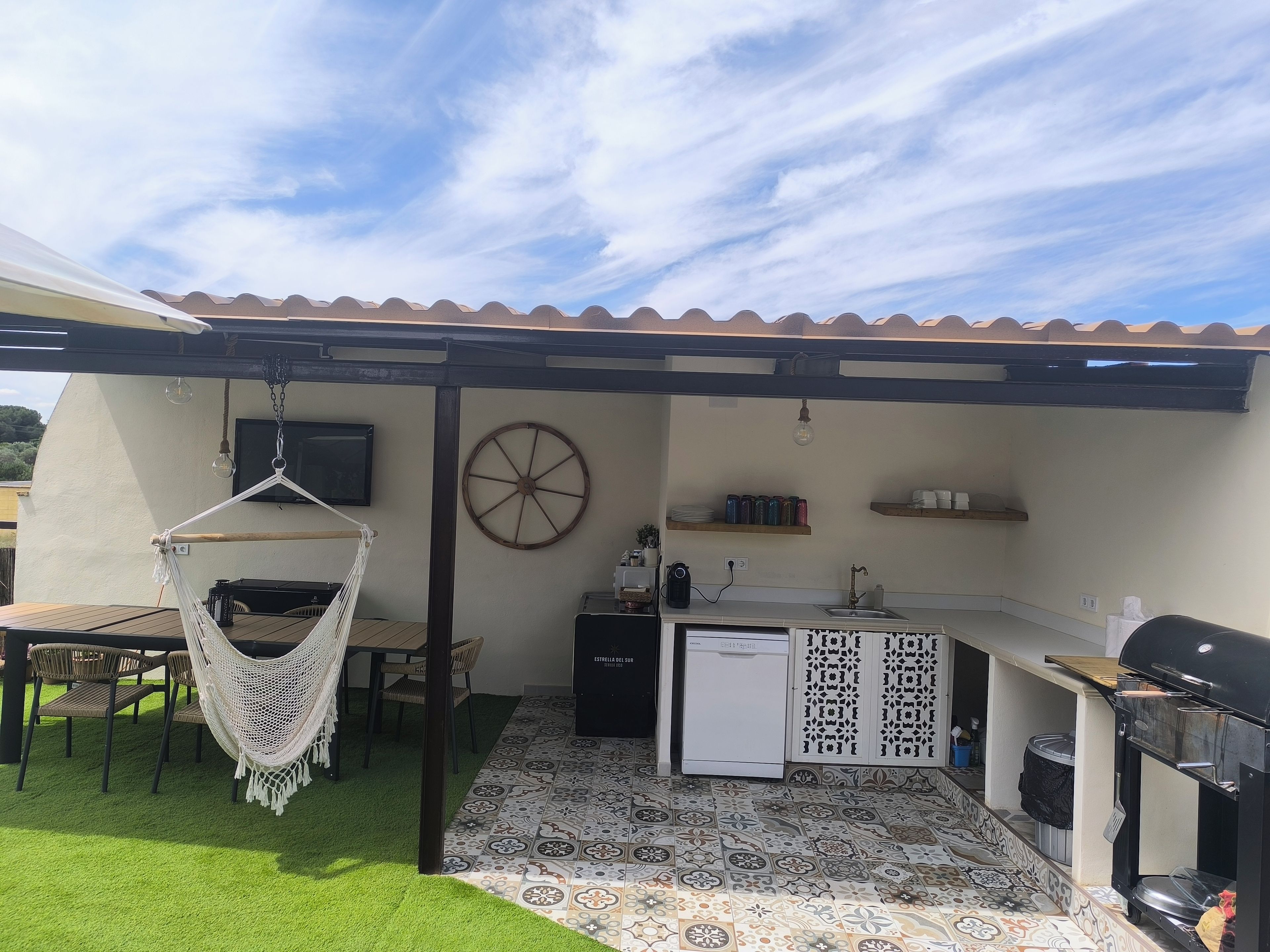 A patio with a hammock, a small kitchenette, and a dining area with a table and chairs.