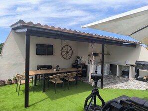 An outdoor patio with a table and chairs, a hanging light fixture, and a wheelbarrow.