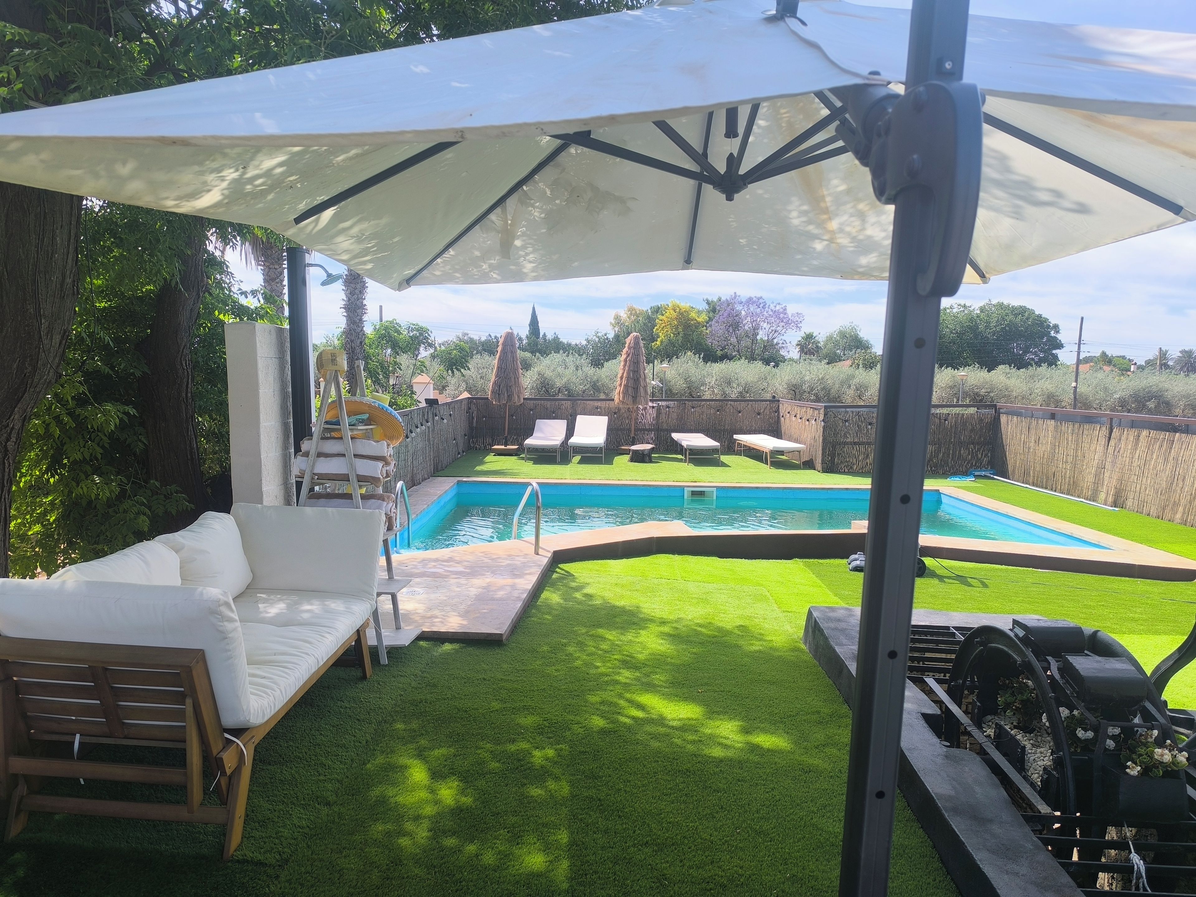 Un patio trasero con piscina, una zona de estar cubierta y un jardín.