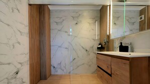 Un baño moderno con paredes de mármol, armarios de madera y cabina de ducha de vidrio.