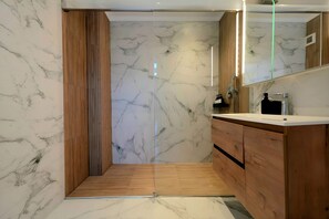 A modern bathroom with marble walls, wooden cabinets, and a glass shower enclosure.