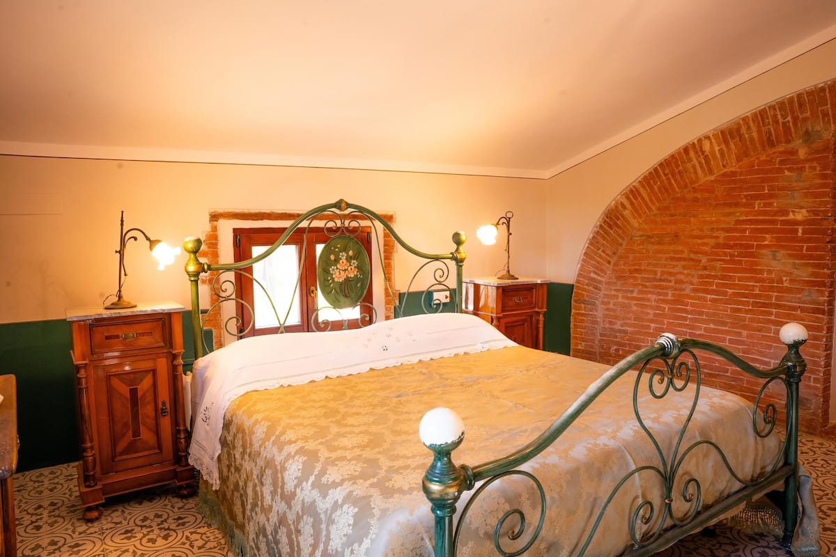 Un dormitorio tradicional con cama con dosel, mesita de noche de madera, pared verde con arco de ladrillo y espejo con diseño floral.
