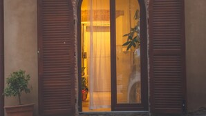 Un bâtiment doté d’une grande porte en arc de cercle, flanquée de deux volets en bois, et d’un pot de fleurs placé à gauche.